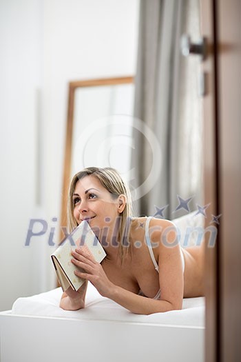 Beautiful young woman in bed, reading her favorite book (shallow DOF, color toned image) Beautiful young woman in bed, reading her favorite book (shallow DOF, color toned image)