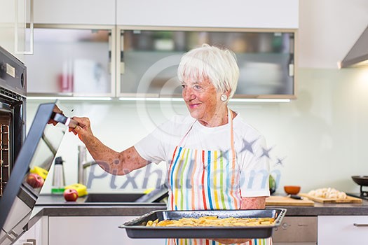 Senior woman cooking in the kitchen - eating and cooking healthy for her family; putting some potates in the oven, enjoying active retirement (shallow DOF; color toned image) Senior woman cooking in the kitchen - eating and cooking healthy for her family; putting some potates in the oven, enjoying active retirement (shallow DOF; color toned image)