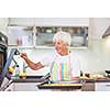 Senior woman cooking in the kitchen - eating and cooking healthy for her family; putting some potates in the oven, enjoying active retirement (shallow DOF; color toned image)