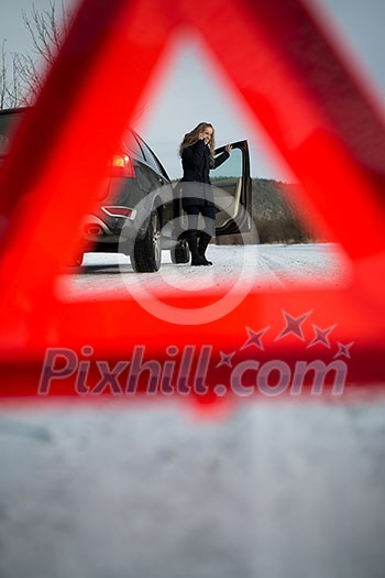 Young woman setting up a warning triangle and calling for assistance after her car broke down in the middle of nowhere on a freezing winter day Young woman setting up a warning triangle and calling for assistance after her car broke down in the middle of nowhere on a freezing winter day
