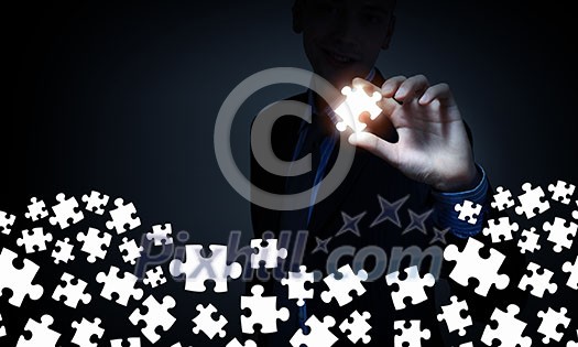 Businesserson on dark background taking puzzle element with fingers Businesserson on dark background taking puzzle element with fingers