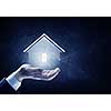 Hand of businessman on dark background showing glowing house sign