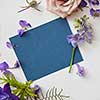 Frame of spring flowers with a blue piece of paper under the text, flat lay