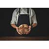 baker in an apron holds bread in hands on a black background