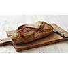 Rye oval bread on a cutting board with a knife on a white background