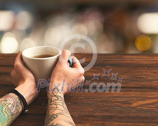 On a wooden brown table a cup of green tea in female hands On a wooden brown table a cup of green tea in female hands