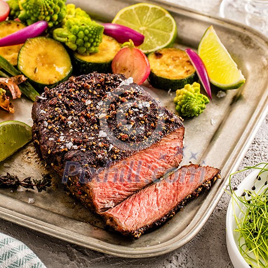 A grilled pepper steak garnished with lemon, onion and fresh herbs. A grilled pepper steak garnished with lemon, onion and fresh herbs.