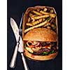 Fresh homemade hamburger with fried potatoes packed in a box on a black background. Top view. Retro vintage toned.