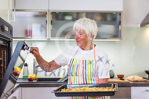 Senior woman cooking in the kitchen - eating and cooking healthy for her family; putting some potates in the oven, enjoying active retirement (shallow DOF; color toned image) Senior woman cooking in the kitchen - eating and cooking healthy for her family; putting some potates in the oven, enjoying active retirement (shallow DOF; color toned image)