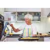 Senior woman cooking in the kitchen - eating and cooking healthy for her family; putting some potates in the oven, enjoying active retirement (shallow DOF; color toned image)