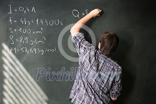College student solving a math problem during math class in front of the blackboard/chalkboard (color toned image) College student solving a math problem during math class in front of the blackboard/chalkboard (color toned image)
