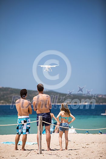 Young people flying a drone by remote control on a beach/sea shore, enjoying summer vacation.