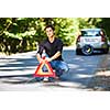 Handsome young man with his car broken down by the roadside, setting the safety triangle