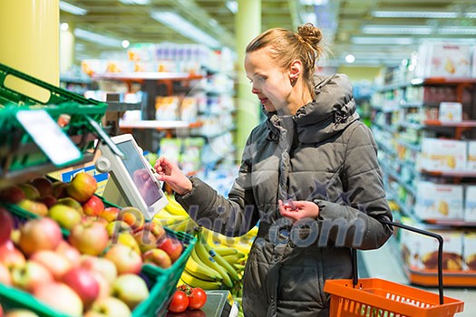 Beautiful, young woman shopping for fruits and vegetables in produce department of a grocery store/supermarket (shallow DOF; color toned image)