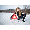 Young woman setting up a warning triangle and calling for assistance after her car broke down in the middle of nowhere on a freezing winter day