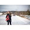 Young woman setting up a warning triangle and calling for assistance after her car broke down in the middle of nowhere on a freezing winter day