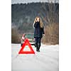 Young woman setting up a warning triangle and calling for assistance after her car broke down in the middle of nowhere on a freezing winter day