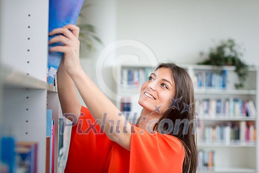 Pretty, young college student looking for a book in the library, studying for her exam Pretty, young college student looking for a book in the library, studying for her exam
