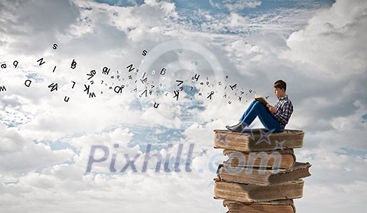 Teenager sitting on pile of books and reading Teenager sitting on pile of books and reading