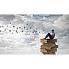 Teenager sitting on pile of books and reading