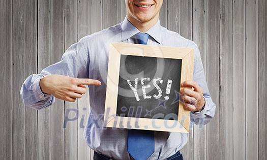 Young smiling businessman holding chalkboard with yes word Young smiling businessman holding chalkboard with yes word