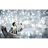 Young angry businessman sitting on chair and screaming in megaphone