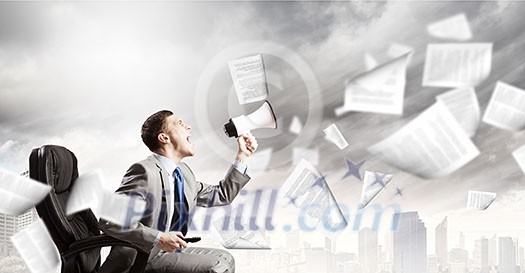 Young angry businessman sitting on chair and screaming in megaphone Young angry businessman sitting on chair and screaming in megaphone