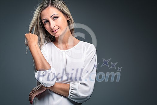 Portrait of a very attractive blonde, young woman on grey background, touching her lovely hair, looking both relaxed and confident (color toned image) Portrait of a very attractive blonde, young woman on grey background, touching her lovely hair, looking both relaxed and confident (color toned image)