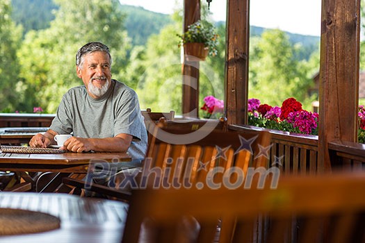 Handsome senior man enjoying his morning coffee on a mountain hotel terrace, while on vacation