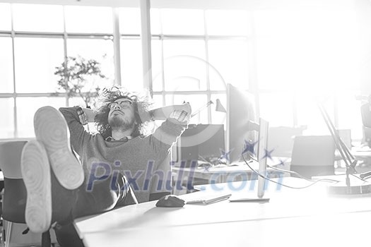Full length of a relaxed casual young businessman sitting with legs on desk at office Full length of a relaxed casual young businessman sitting with legs on desk at office