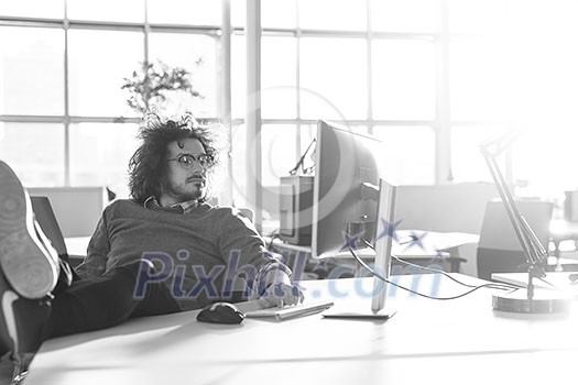 Full length of a relaxed casual young businessman sitting with legs on desk at office Full length of a relaxed casual young businessman sitting with legs on desk at office