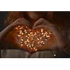 Female hands holding a Christmas string of lights in the form of a heart on a dark background