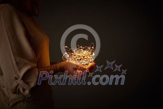in the hands of a woman a Christmas garland of lights on a dark background in the hands of a woman a Christmas garland of lights on a dark background