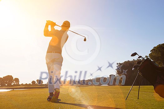 golf player hitting shot with club on course at beautiful morning with sun flare in background