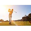 golf player hitting shot with club on course at beautiful morning with sun flare in background