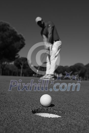 golf player hitting shot with driver, ball on edge of hole on course in background at beautiful sunny day golf player hitting shot with driver, ball on edge of hole on course in background at beautiful sunny day