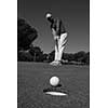 golf player hitting shot with driver, ball on edge of  hole  on course in background  at beautiful sunny day