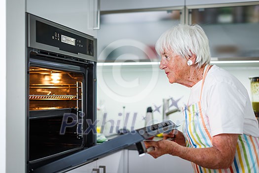 Senior woman cooking in the kitchen - eating and cooking healthy for her family; putting some potates in the oven, enjoying active retirement (shallow DOF; color toned image) Senior woman cooking in the kitchen - eating and cooking healthy for her family; putting some potates in the oven, enjoying active retirement (shallow DOF; color toned image)