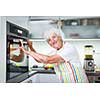 Senior woman cooking in the kitchen - eating and cooking healthy for her family; putting some potates in the oven, enjoying active retirement (shallow DOF; color toned image)