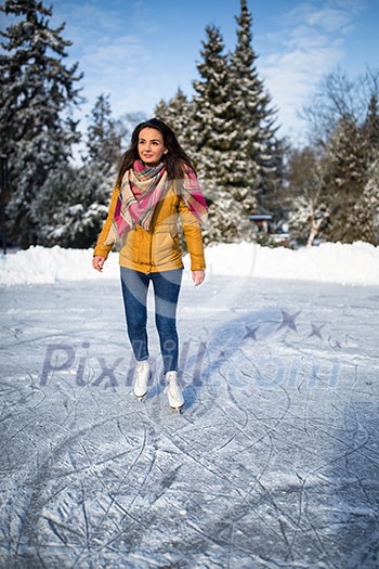 Young woman ice skating outdoors on a pond on a freezing winter day (color toned image; motion blurred image)