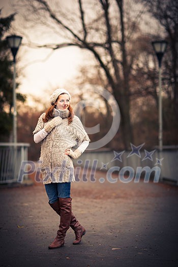 Autumn/winter portrait: young woman dressed in a warm woolen cardigan posing outside in a city park