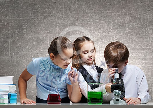 Three cute children at chemistry lesson making experiments Three cute children at chemistry lesson making experiments