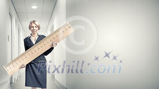 Young businesswoman measuring something with big ruler Young businesswoman measuring something with big ruler