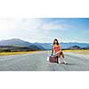 Traveler woman sits on retro suitcase and waiting for car