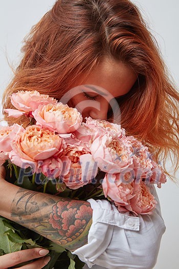 pretty red-haired girl with a tattoo on her arm holding and smell a bouquet of pink roses, valentine's day, mother's day