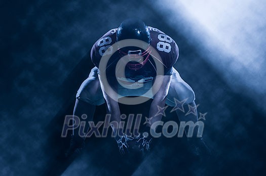 American football player starting football game on big modern american football field with lights and flares at night American football player starting football game on big modern american football field with lights and flares at night