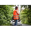 Young female driver wearing a high visibility vest, calling the roadside service/assistance after her car has broken down
