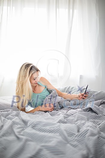 Beautiful young woman in bed, taking a selfie on her cell phone (color toned image; shallow DOF) Beautiful young woman in bed, taking a selfie on her cell phone (color toned image; shallow DOF)