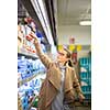 Beautiful young woman shopping for groceries and fruits and vegetables in produce department as well as some lactose free diary products in a modern grocery store/supermarket (color toned image; shallow DOF)