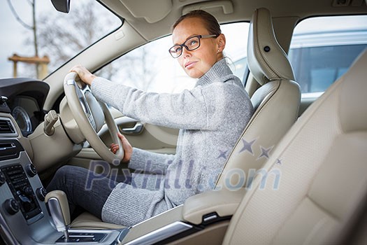Woman driving a car - female driver at a wheel of a modern car, looking happy, smiling with a relaxed smile (shallow DOF; color toned image) Woman driving a car - female driver at a wheel of a modern car, looking happy, smiling with a relaxed smile (shallow DOF; color toned image)